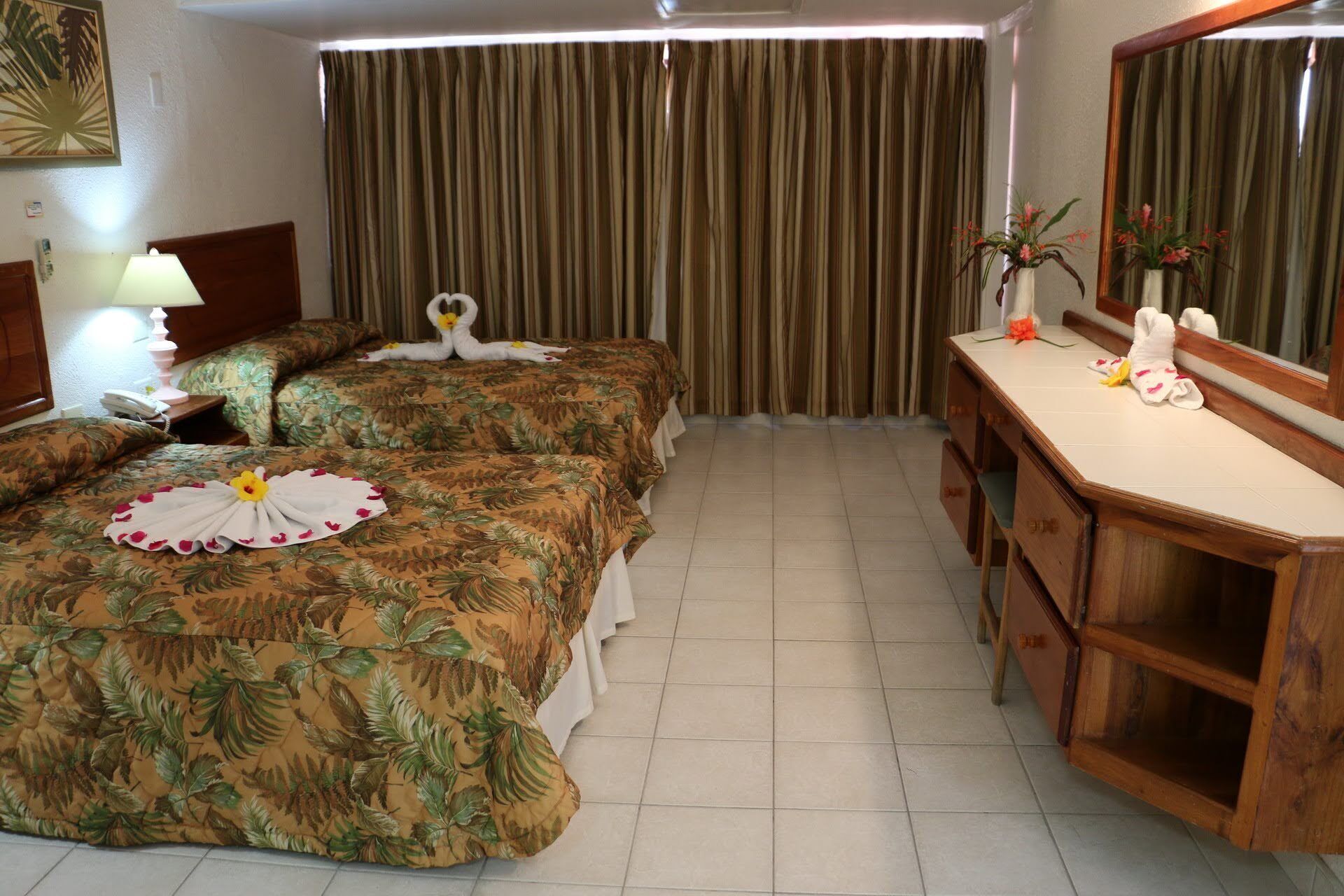 Una habitación de hotel con dos camas, un aparador de madera, un espejo y una cortina.