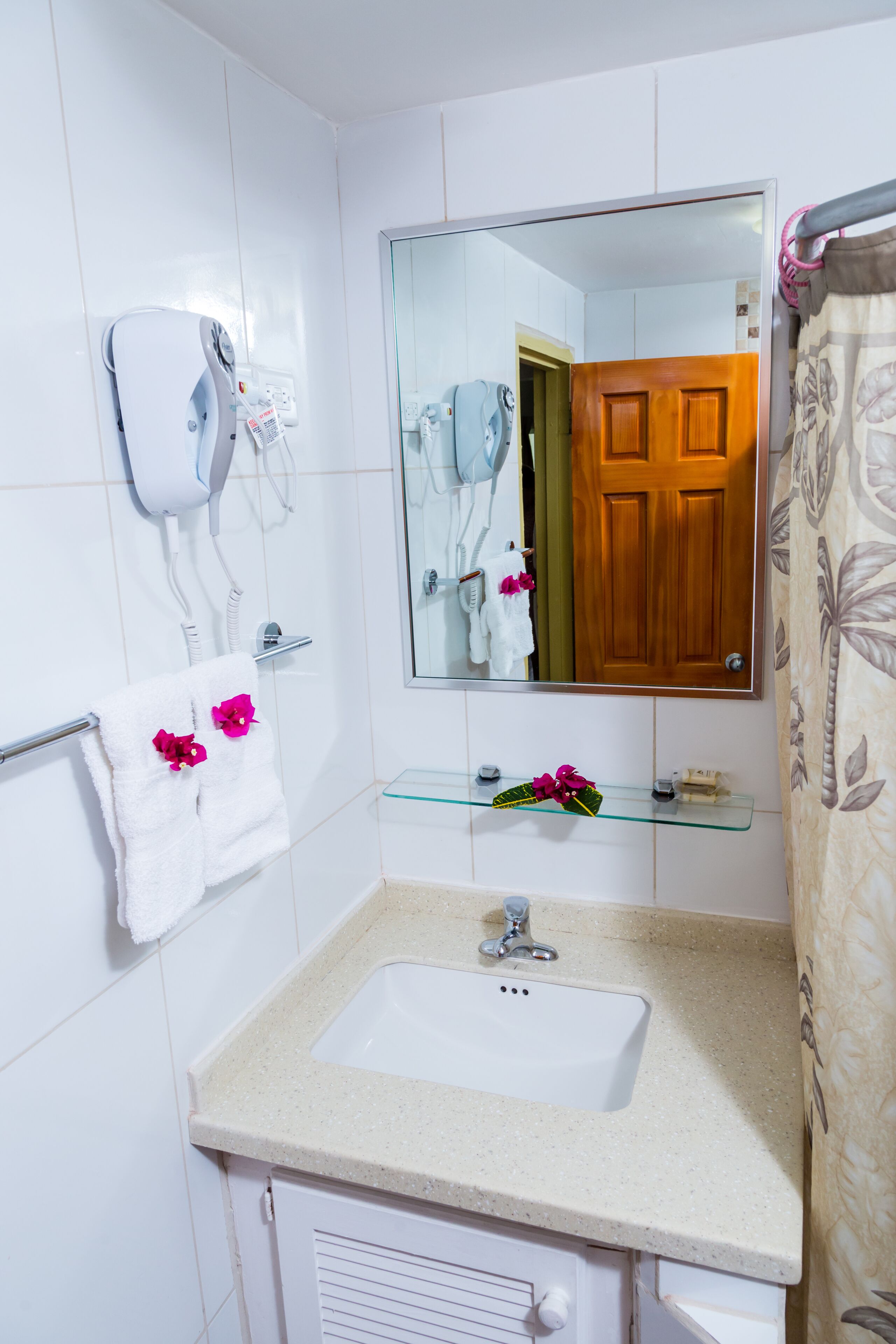 A bathroom with a white sink, a mirror, a towel rack with towels, a hairdryer, and a shower curtain.