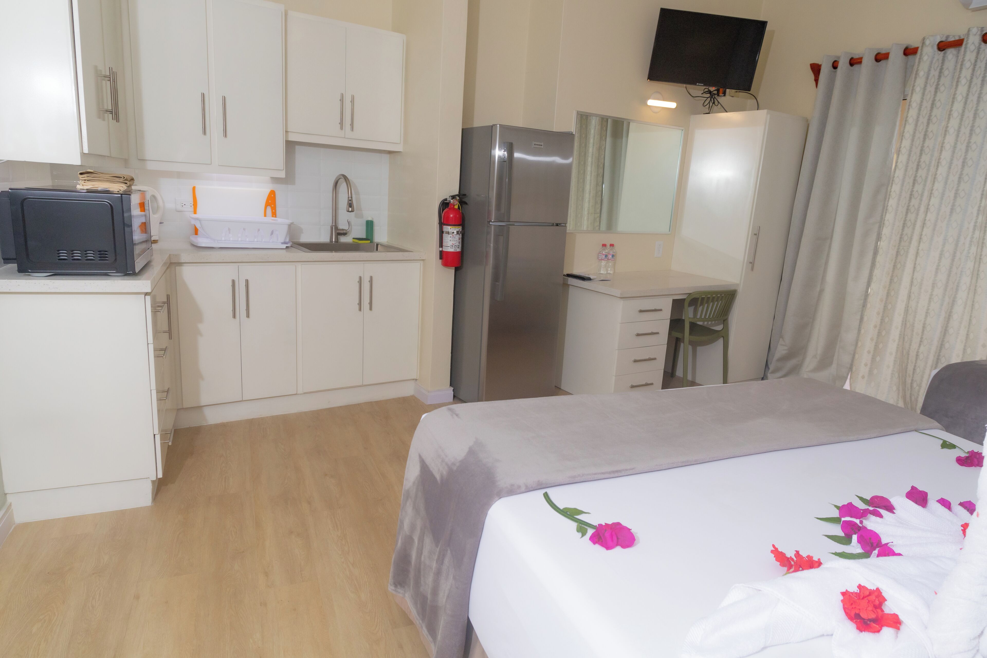 Una habitación de hotel compacta con kitchenette, una cama con ropa de cama floral, un televisor y un baño con cortina de ducha.