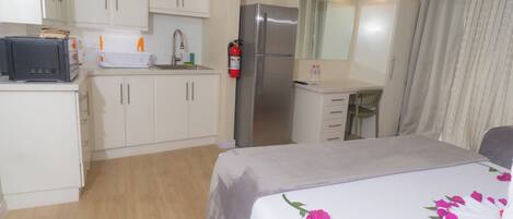Una habitación de hotel compacta con kitchenette, una cama con ropa de cama floral, un televisor y un baño con cortina de ducha.