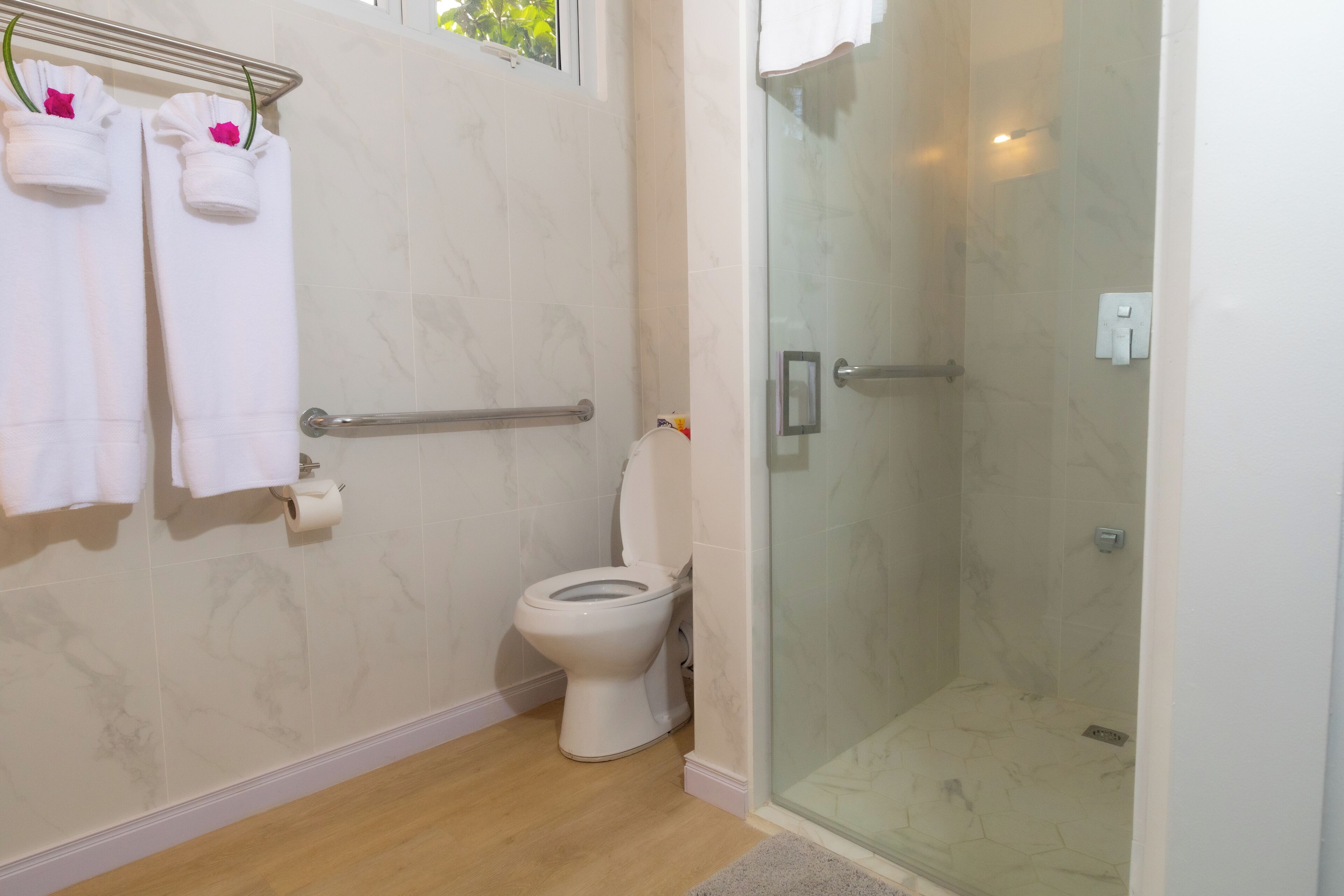 Une salle de bain avec des toilettes, une douche dotée d’une porte en verre et des serviettes suspendues sur un porte-serviettes.