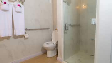 Une salle de bain avec des toilettes, une douche dotée d’une porte en verre et des serviettes suspendues sur un porte-serviettes.
