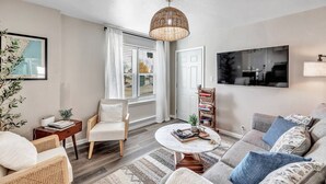 A modern living room with a sofa, armchair, and coffee table. There is a bookshelf and a large window with curtains. - Newly Renovated - Must Stay at in Algoma (Algoma)