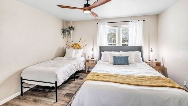 A bedroom with a bed, a smaller bed, a ceiling fan, a window with curtains, and a nightstand with a lamp. - Across the Street From Von Stiehl-newly Renovated (Algoma)