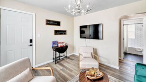 A living room with a white door, a chandelier, a television mounted on the wall, and a small table with books and a basket. - Across the Street From Von Stiehl-newly Renovated (Algoma)