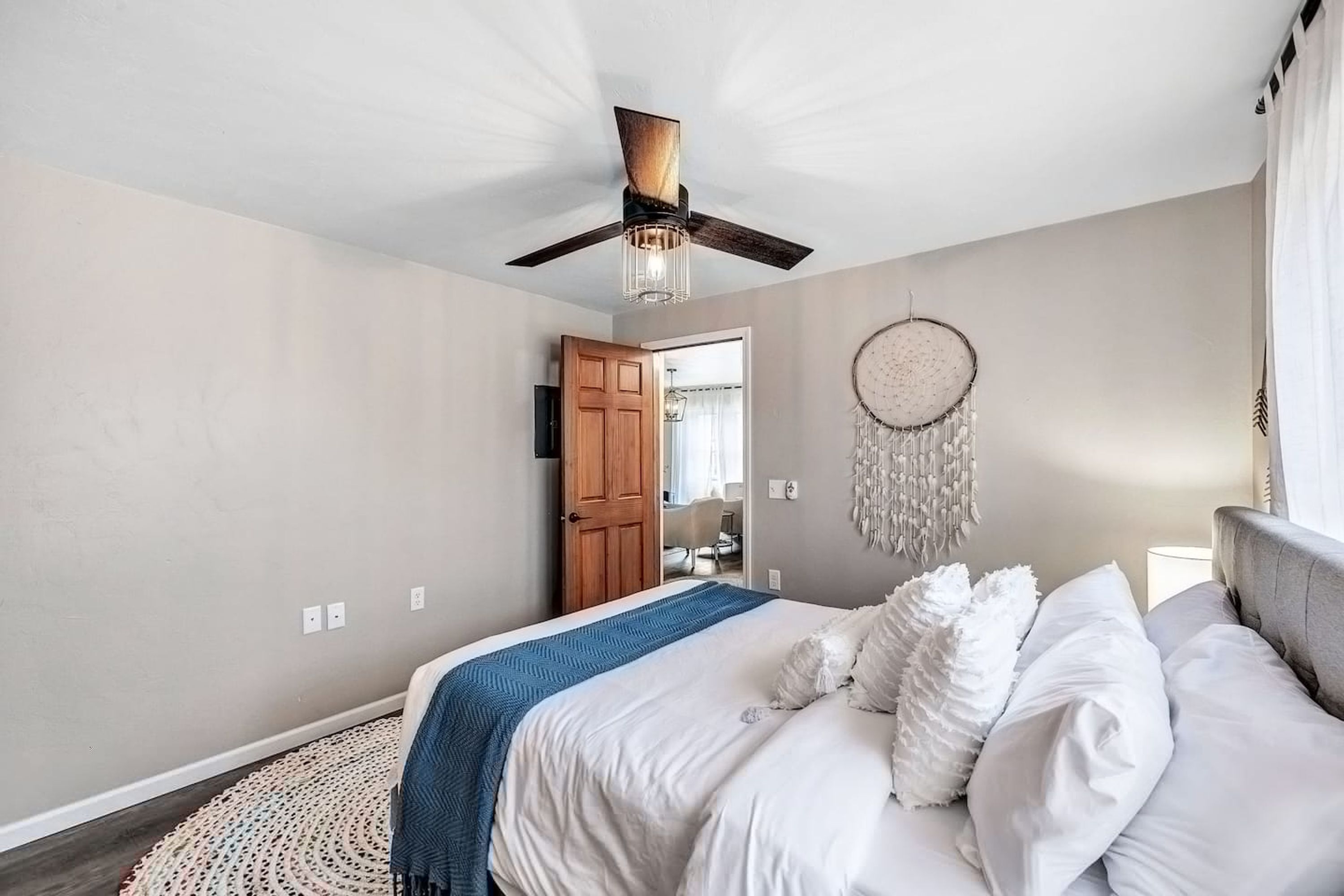 A bedroom with a bed, a ceiling fan, a dreamcatcher, and a round rug.