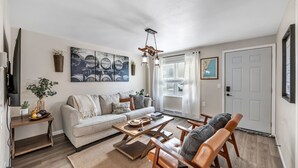 A living room with a sofa, coffee table, and chairs. There is a TV on a stand, a plant, and artwork on the walls. - Newly Renovated - Walking Distance to Pier (Algoma)