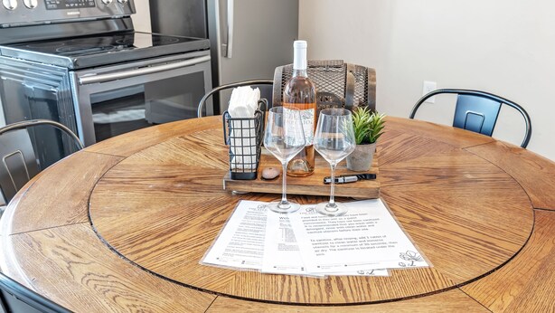 A round wooden table with a menu, two wine glasses, a bottle of wine, a small plant, and a basket with a napkin. - Newly Renovated - Walking Distance to Pier (Algoma)