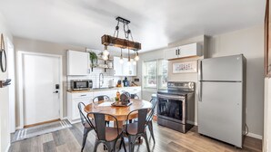 A modern kitchen with a wooden dining table, black chairs, a hanging light fixture, and stainless steel appliances. - Newly Renovated - Walking Distance to Pier (Algoma)