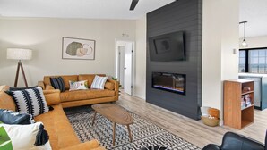 A modern living room with a sofa, coffee table, fireplace, and a ceiling fan.