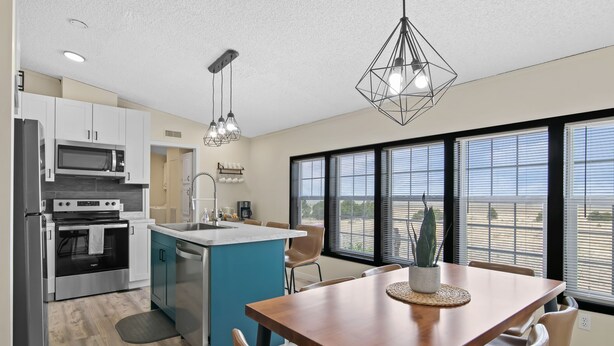 A modern kitchen with a central island, stainless steel appliances, and a dining area with a wooden table and chairs.