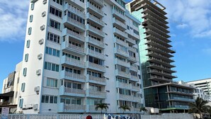 A multi-story hotel with balconies, a sandy beach in the foreground, and a clear blue sky.