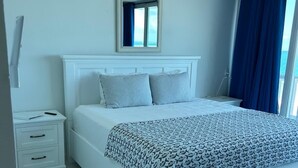 A bedroom with a large bed, a nightstand, a dresser, and a window with curtains.