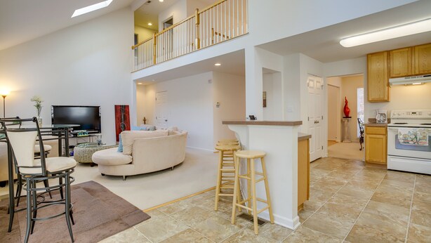 Un salon spacieux avec un canapé, un coin repas avec des chaises, une cuisine équipée d’une cuisinière et un balcon avec une balustrade.