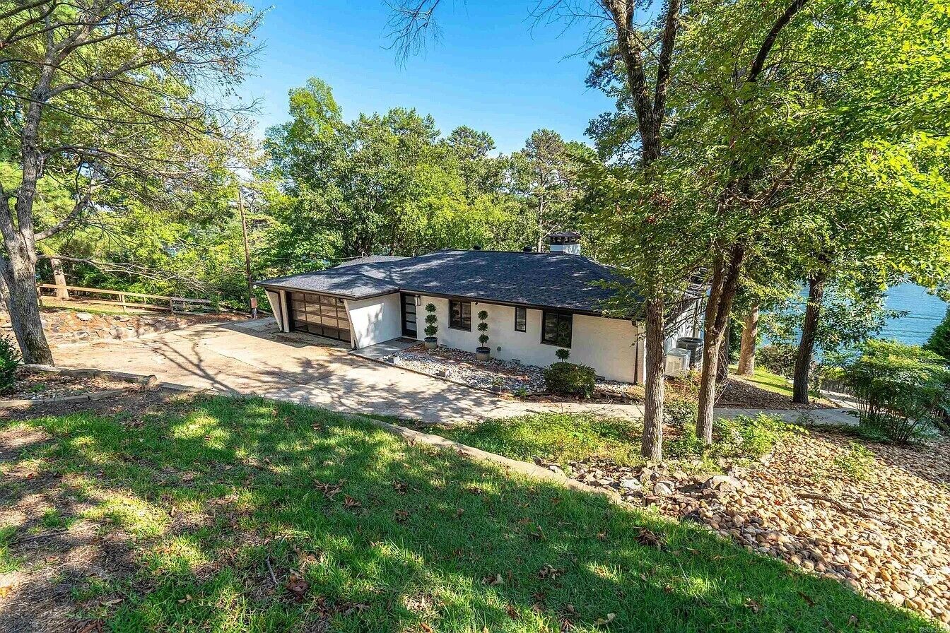 A house with a covered porch, surrounded by trees and a view of a body of water.