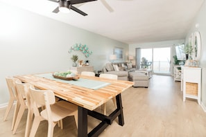 A dining area with a wooden table and chairs, a ceiling fan, and a view to the living room.