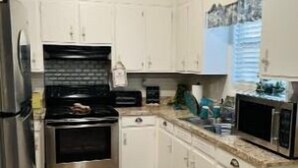 A compact kitchen with white cabinets, a stainless steel stove, a microwave, and a refrigerator.