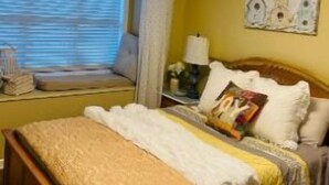A hotel room with a bed, a bedside table, a lamp, and a window with curtains.