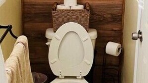 A small bathroom with a wooden wall, a toilet, and a shelf with a floral box and towels.