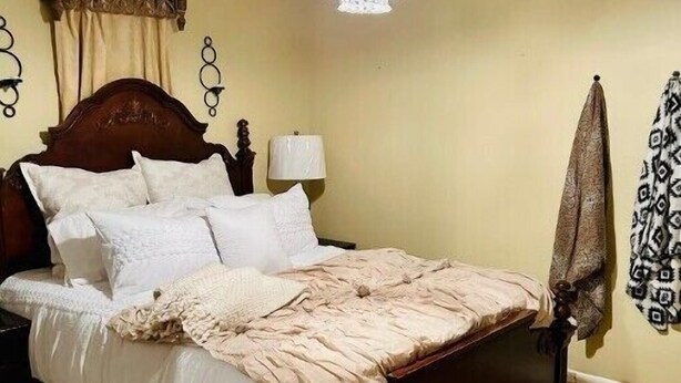 A bedroom with a wooden bed, a chandelier, a nightstand, and a patterned curtain.
