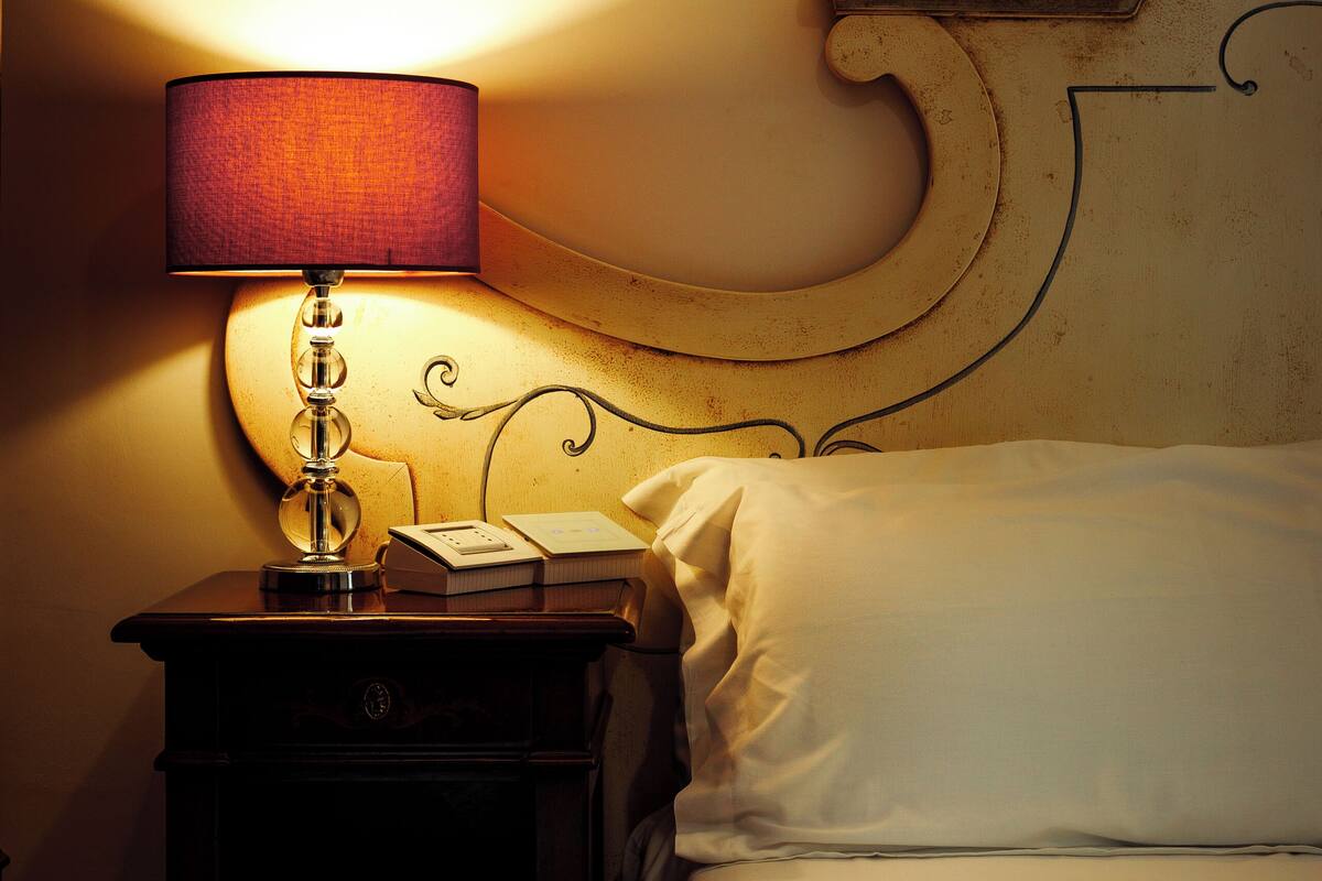 A neatly made bed with a patterned bedspread, a bedside lamp, and a nightstand with a telephone and books.