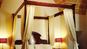 Una cama con dosel y cortinas, dos lámparas de noche y un suelo de baldosas de piedra.