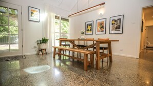 A spacious room with a polished concrete floor, a wooden dining table with benches, and a large window with a view of greenery. - Sanctuary 33 - Your private haven near the river (Bright)