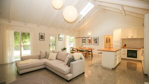 A spacious living area with a large L-shaped sofa, a dining table, and a kitchen with white cabinetry. - Sanctuary 33 - Your private haven near the river (Bright)