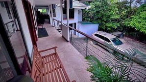 Un balcó amb una banca de fusta, vista a un cotxe estacionat i un jardí amb arbres.