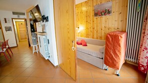 Um quarto com parede de madeira, sofá branco, um objeto coberto, radiador e porta que dá para outro cômodo.