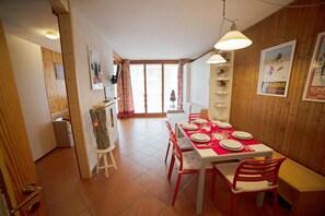Een eethoek met een houten tafel voor vier personen, rode stoelen en een witte bank.