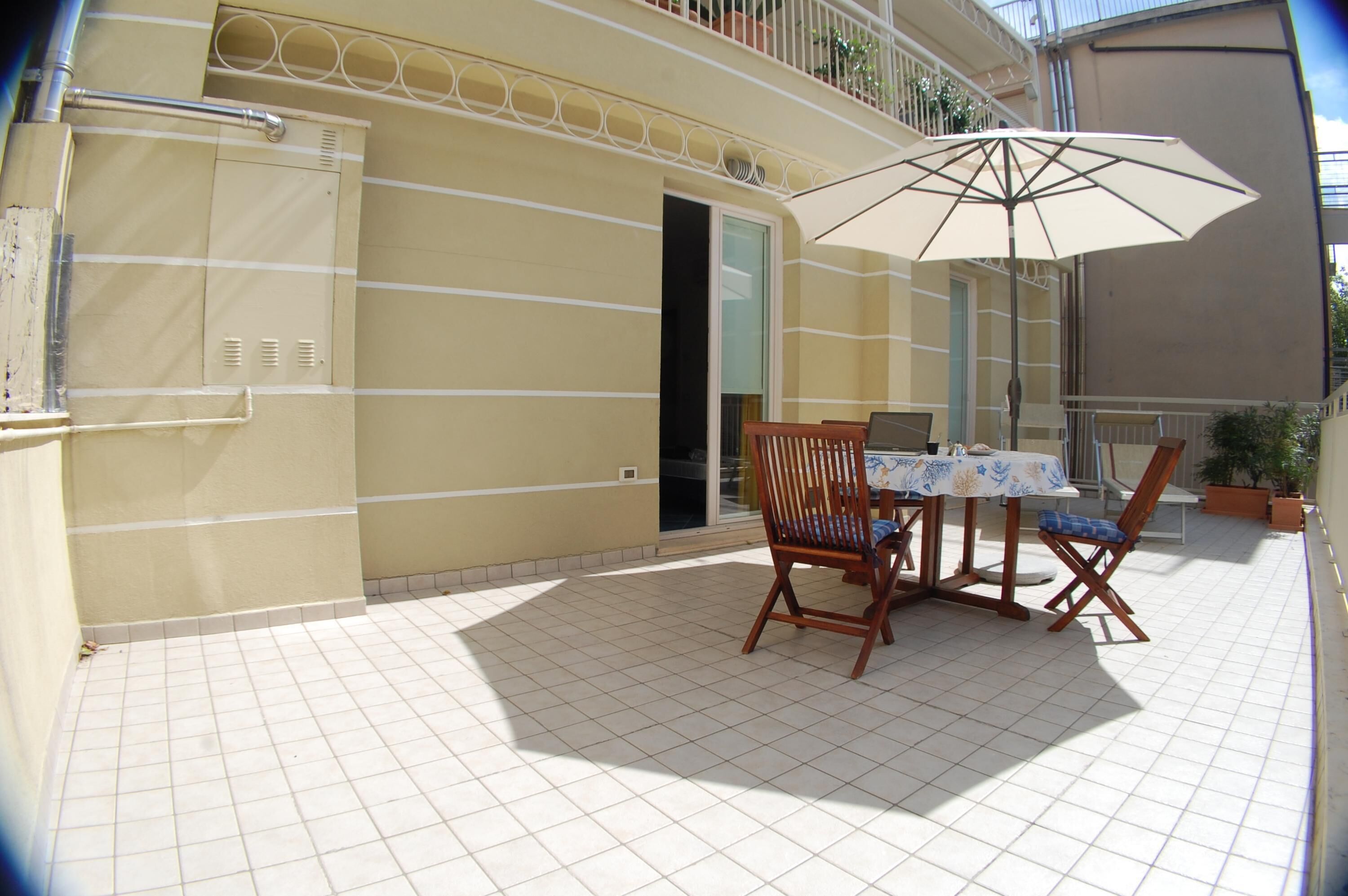 A patio with a table and chairs, an umbrella, and a door leading to a balcony.