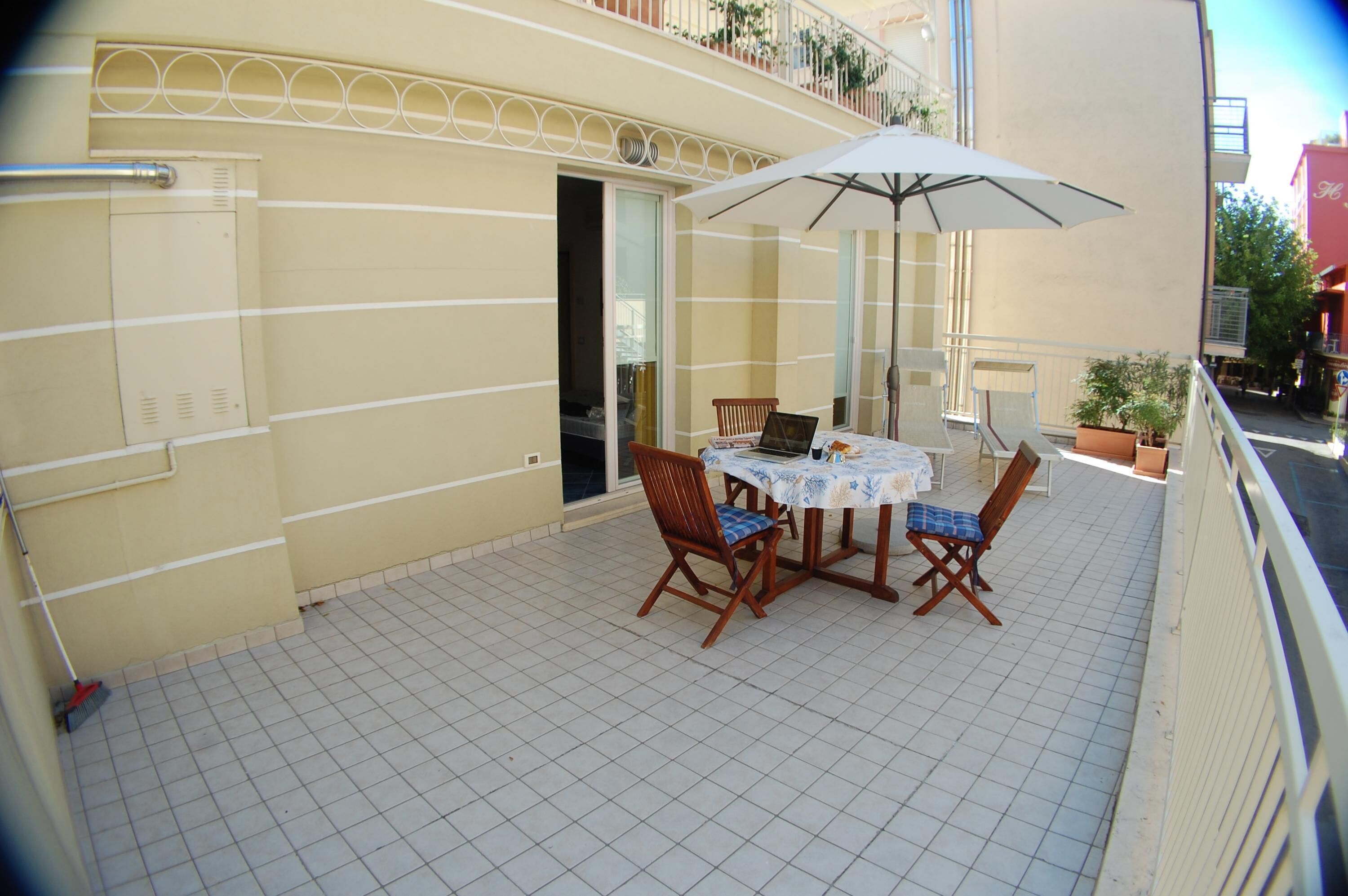 A balcony with a table and chairs, a white umbrella, and a potted plant.