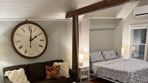 Een gezellig compacte ruimte met een keukenhoek, een eettafel, een bank, een bed en een grote wandklok.