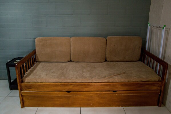 Un sofá cama de madera con un cojín beige frente a una pared con textura.