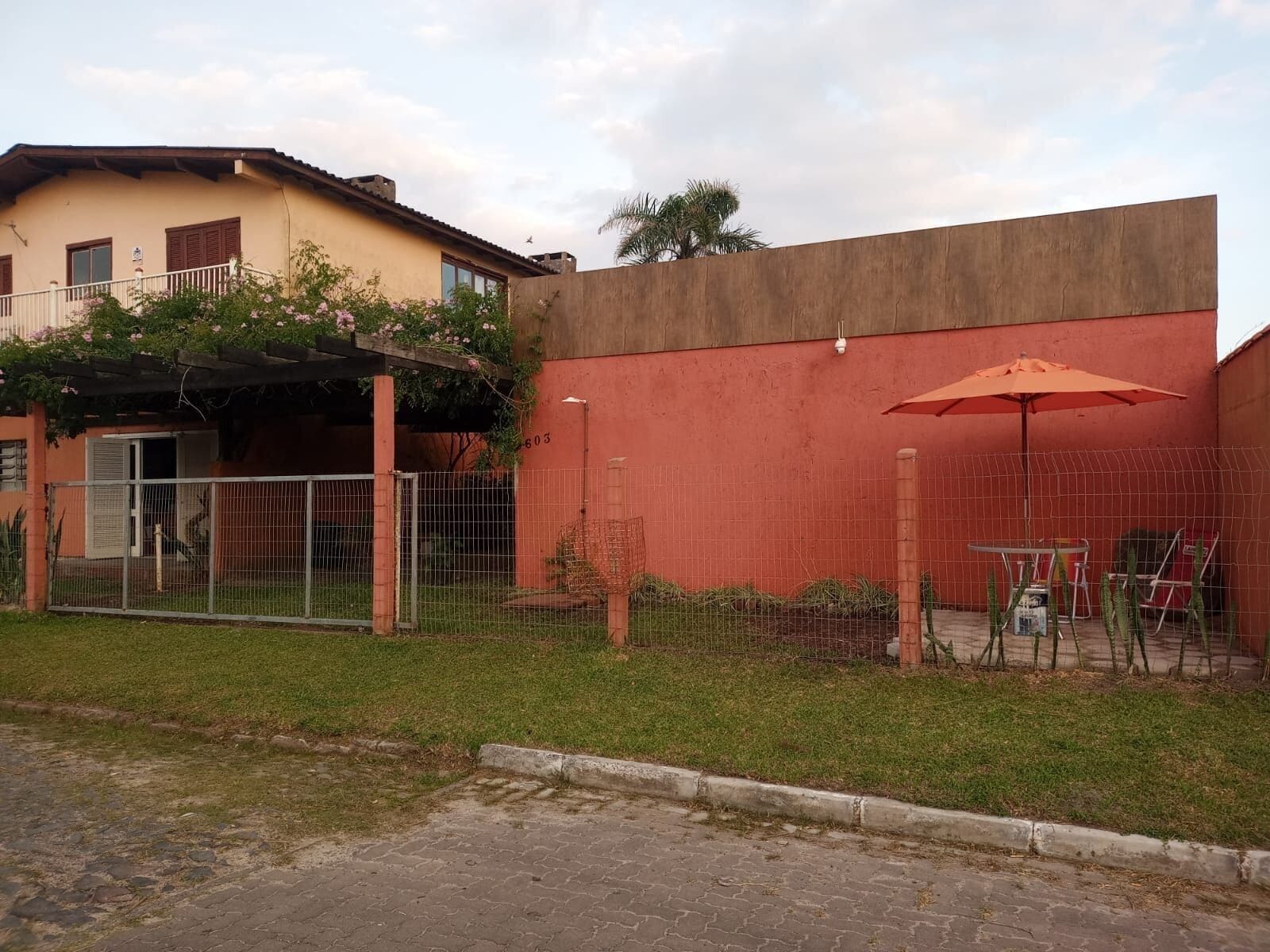 Un edificio de fachada roja, un área cercada con una mesa y sillas, y un pequeño jardín.