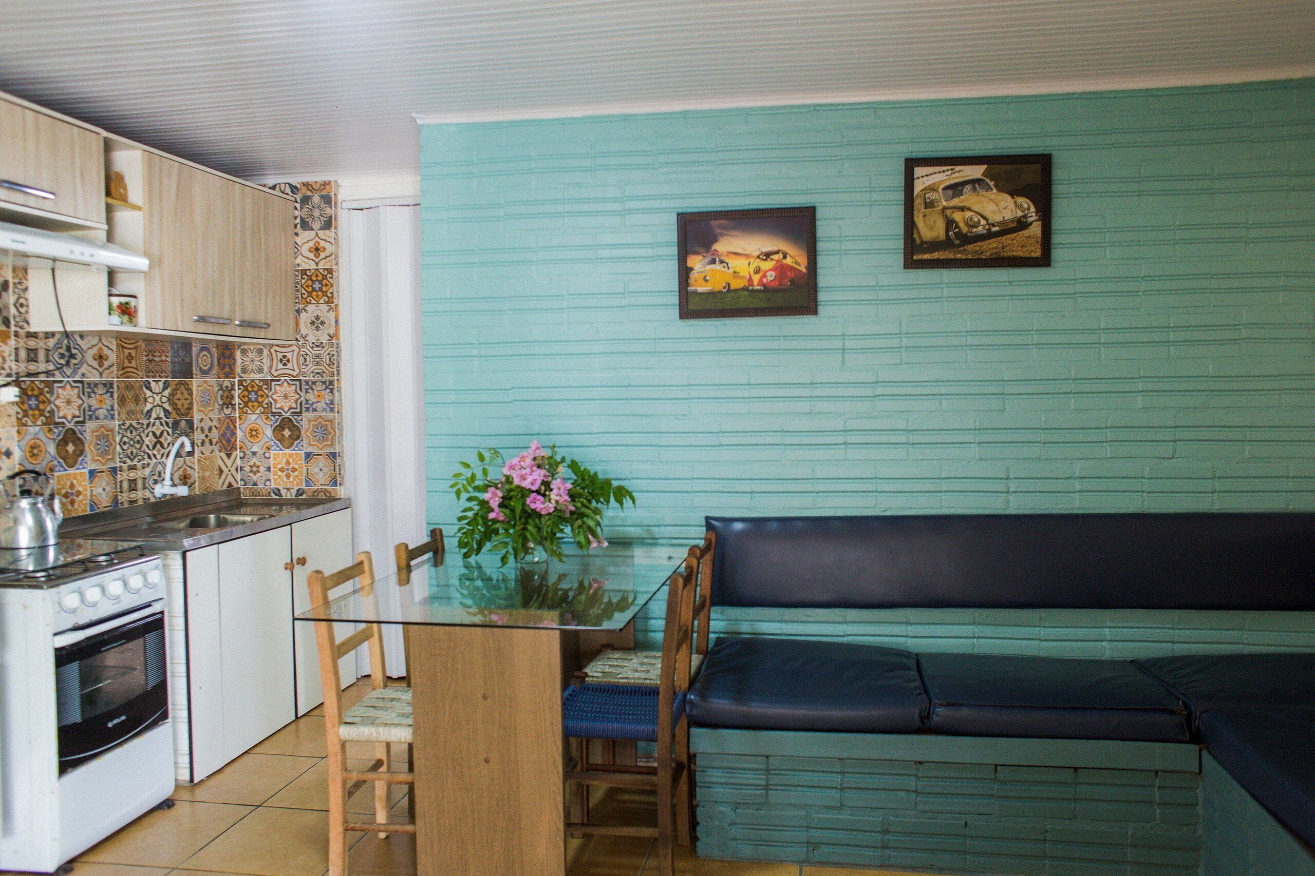 Cocina compacta con estufa, pileta y placares, una mesa de comedor con sillas y un sofá color verde azulado.