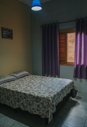 Un dormitorio con cama, ventana con cortinas, un cuadro en la pared y una lámpara en el techo.