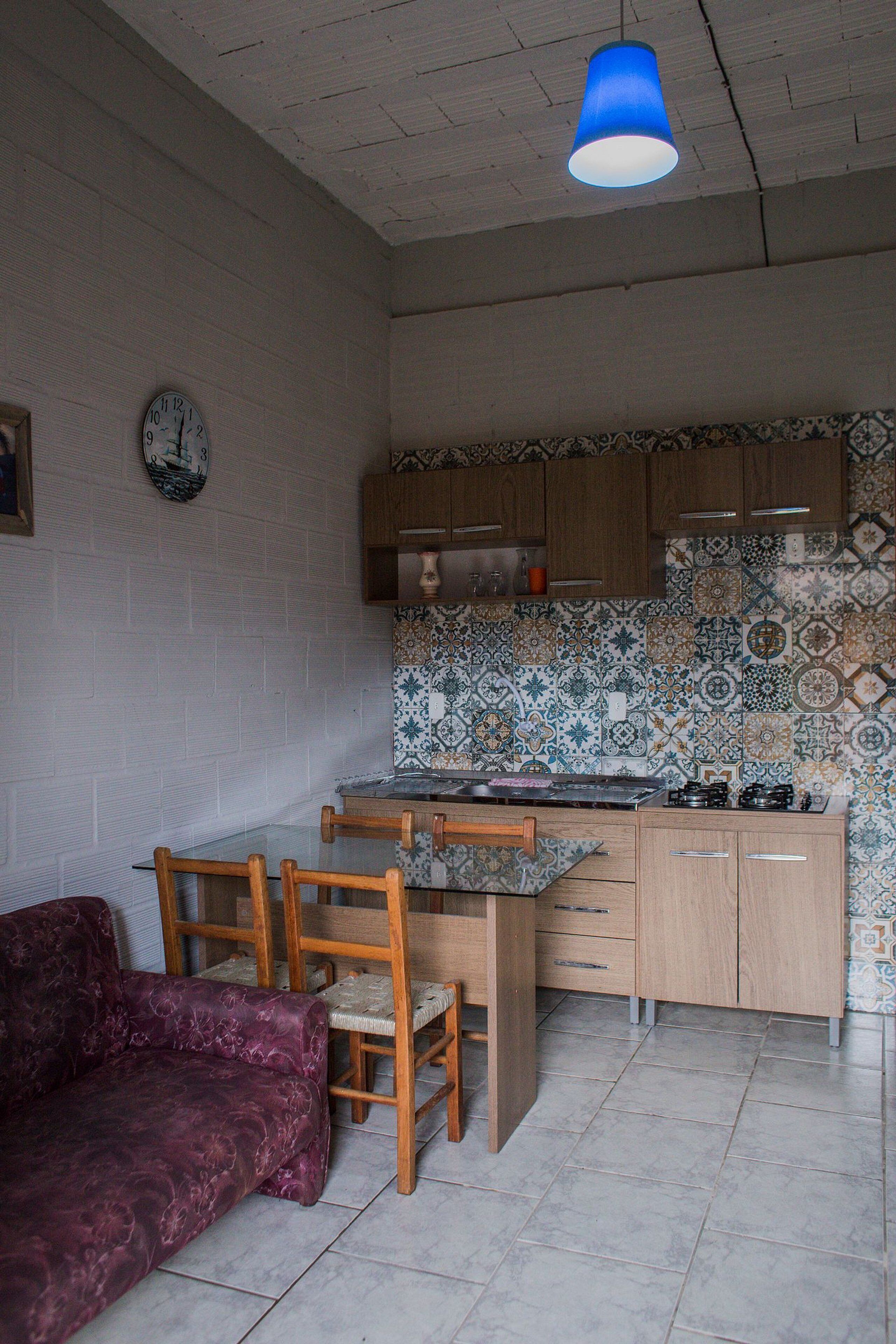 Una cocina compacta con zona de comedor, un reloj en la pared y una lámpara colgante azul.