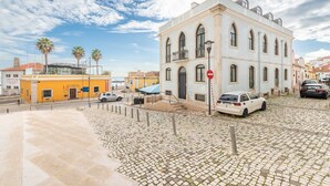 Una calle adoquinada con un edificio histórico, un edificio amarillo y coches estacionados.