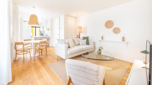 Una sala de estar moderna con una mesa de centro de vidrio, un sofá y un comedor con sillas de madera.