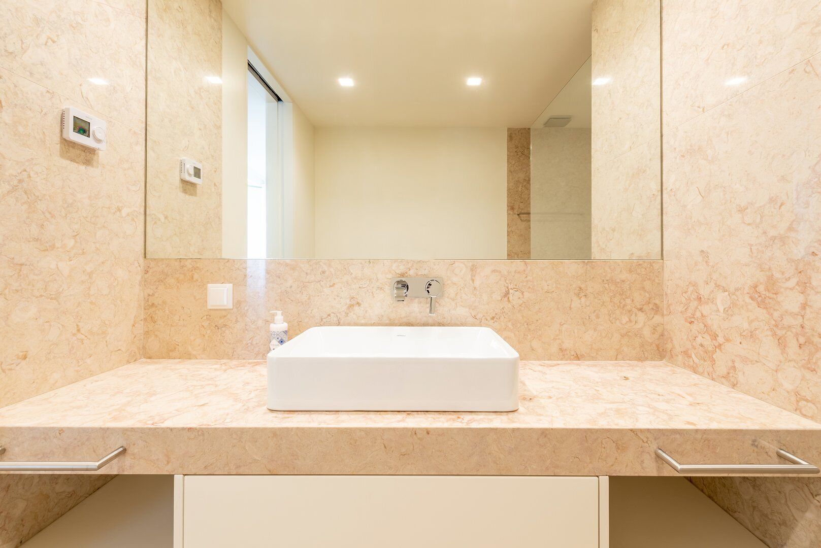 Une salle de bain avec un lavabo blanc, des murs en marbre et un grand miroir.