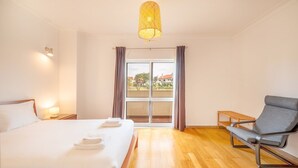 Ein Hotelzimmer mit einem Bett, einem Sessel, einem kleinen Tisch, einer Lampe und Blick ins Freie.