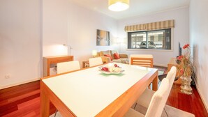 A dining area with a wooden table and chairs, a sofa set, a lamp, and a window with a view of parked cars.