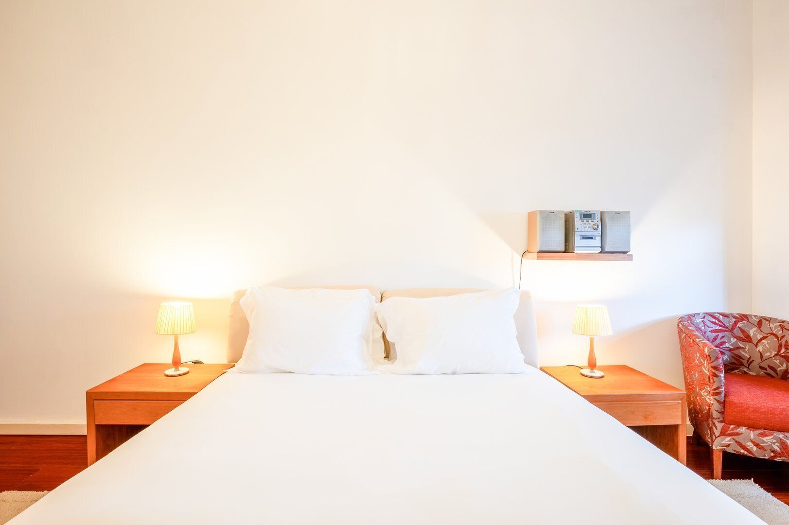 Habitación de hotel con una cama grande, dos mesitas de noche con lámparas, una silla con estampado de hojas y un aire acondicionado instalado en la pared.