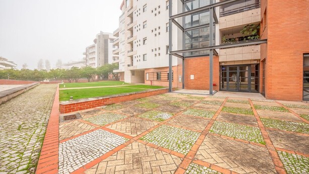 A modern building with a courtyard featuring a patterned tile floor and a grassy area.