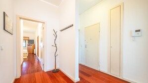 A hallway with wooden flooring, white walls, and a coat rack. There is a door on the right and a door at the end of the hallway.