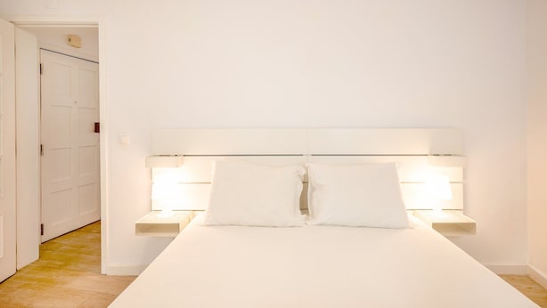 A minimalist bedroom with a large bed, two bedside tables, and a white headboard. - GuestReady - Delightful getaway in the city centre (Lisbon)