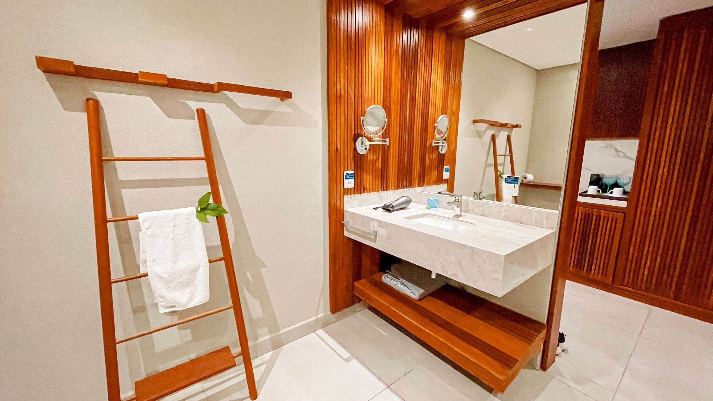 Un baño con una escalera de madera, un lavamanos blanco y un espejo grande.