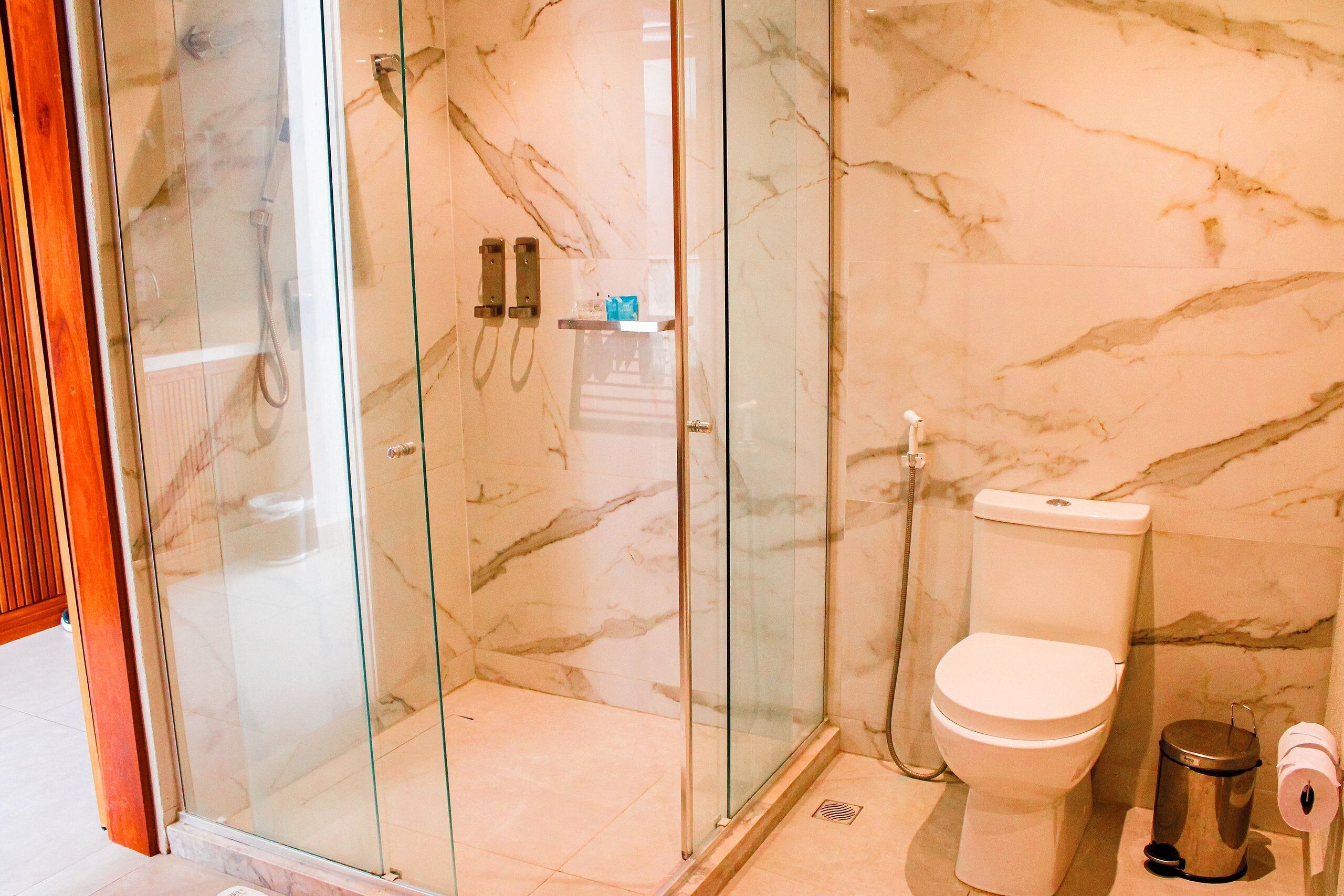 Een badkamer met een douche met glazen wand, een toilet en een prullenbak.
